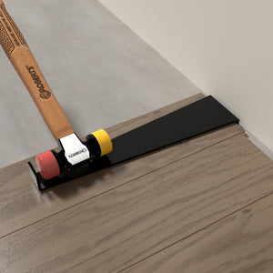 A hammer strikes the tapping block from the Roberts Pro Flooring Installation Kit, aligning the plank with the wall during laminate or vinyl flooring installation.