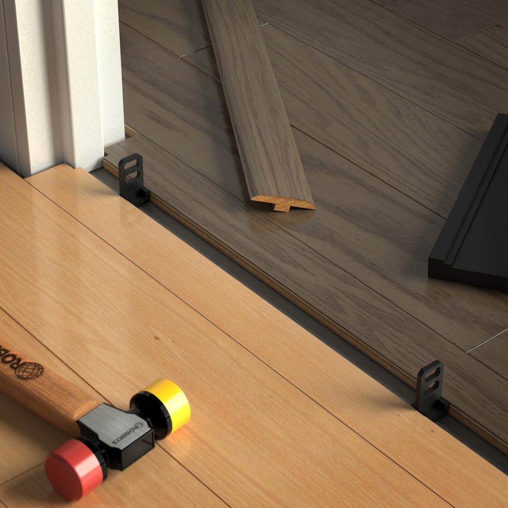 Close-up of two types of wood flooring being joined with a T-molding strip during a laminate flooring installation; also shown are flooring spacers and the colorful-handled mallet from the Roberts Pro Flooring Installation Kit.