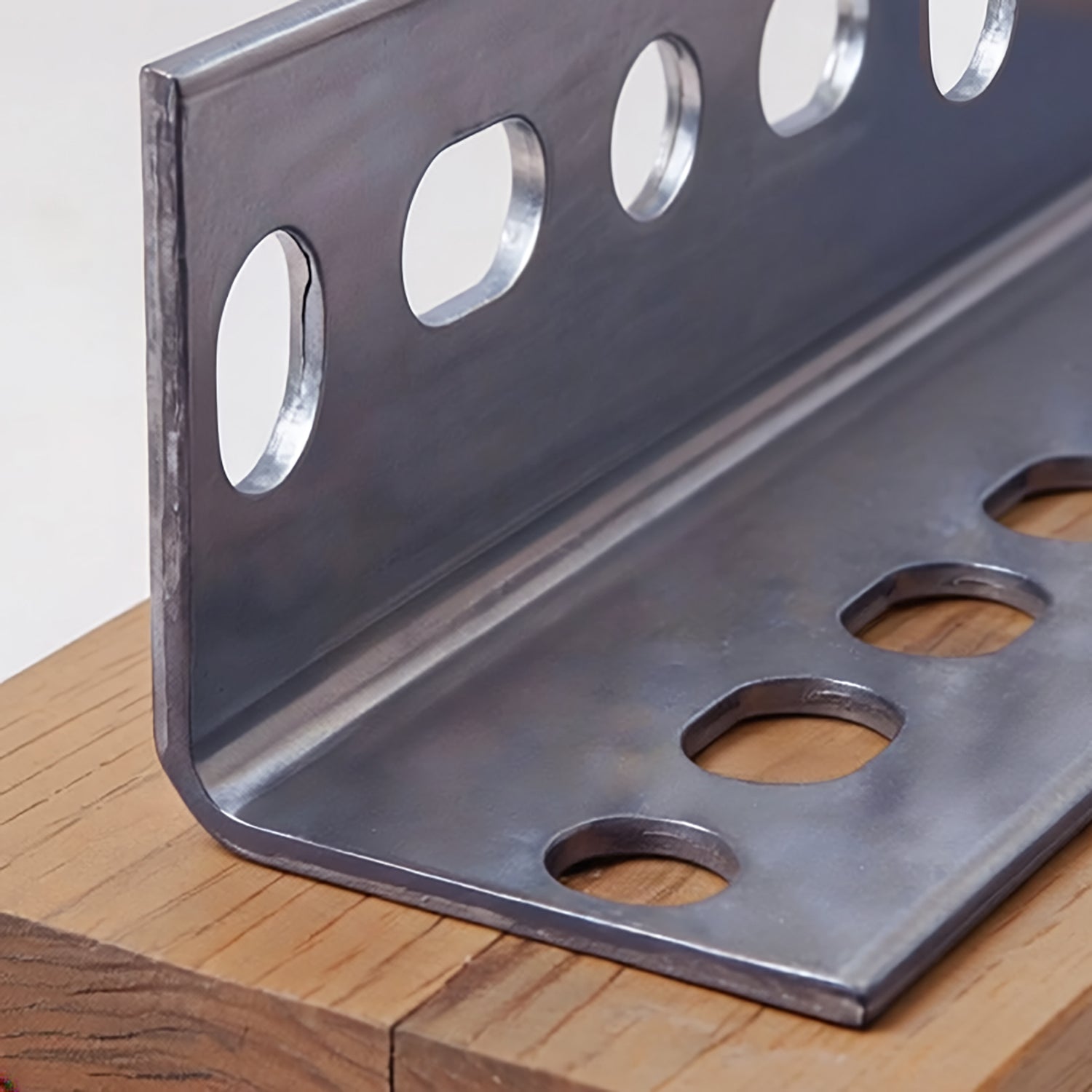 Hillman 1-1/2″ x 36″ Steel Slotted Angle, Galvanized, featuring a heavy-duty angled profile with rows of slotted holes along both sides, resting on a piece of wood.