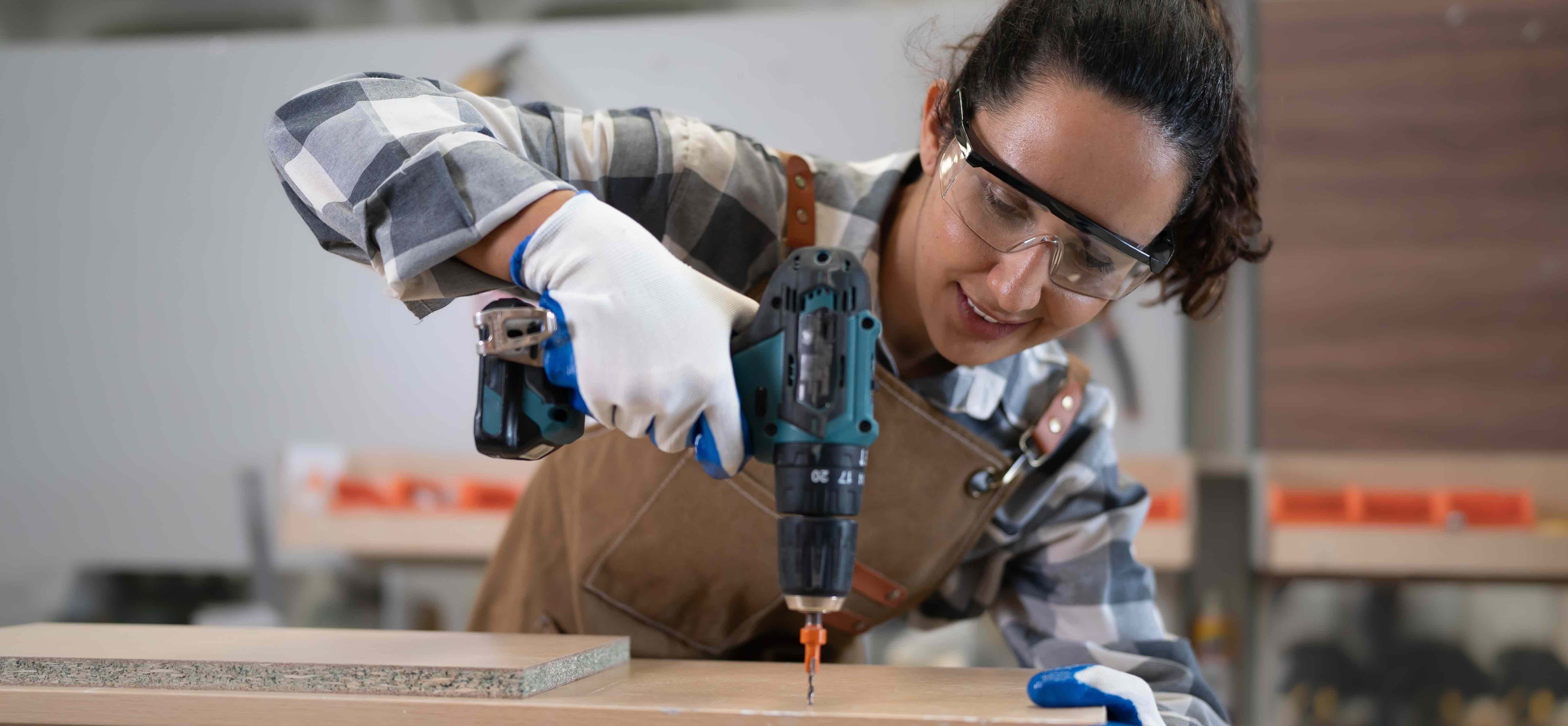 Person using a power drill on a wooden surface in a workshop setting