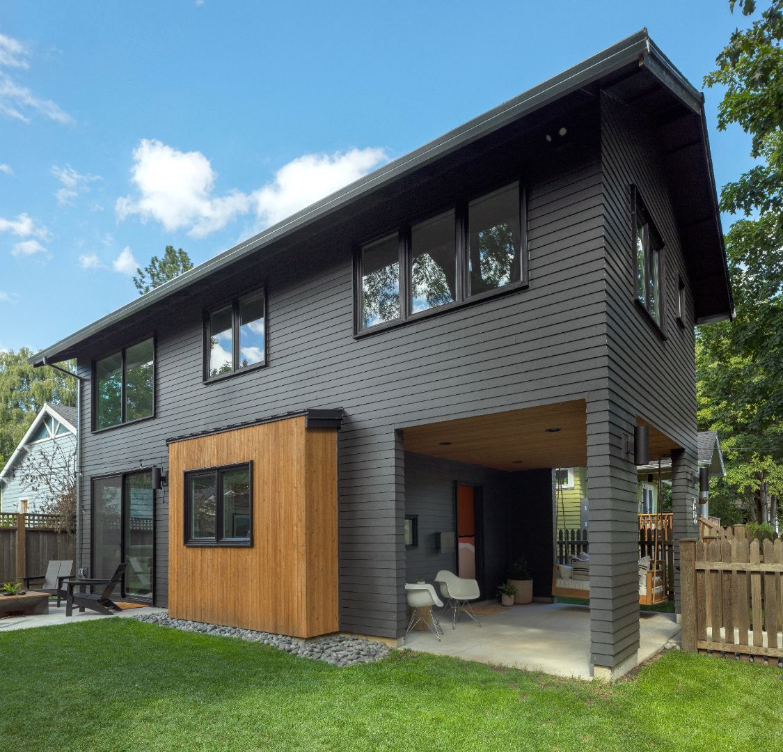 Modern house with gray exterior and wooden accents, surrounded by greenery.