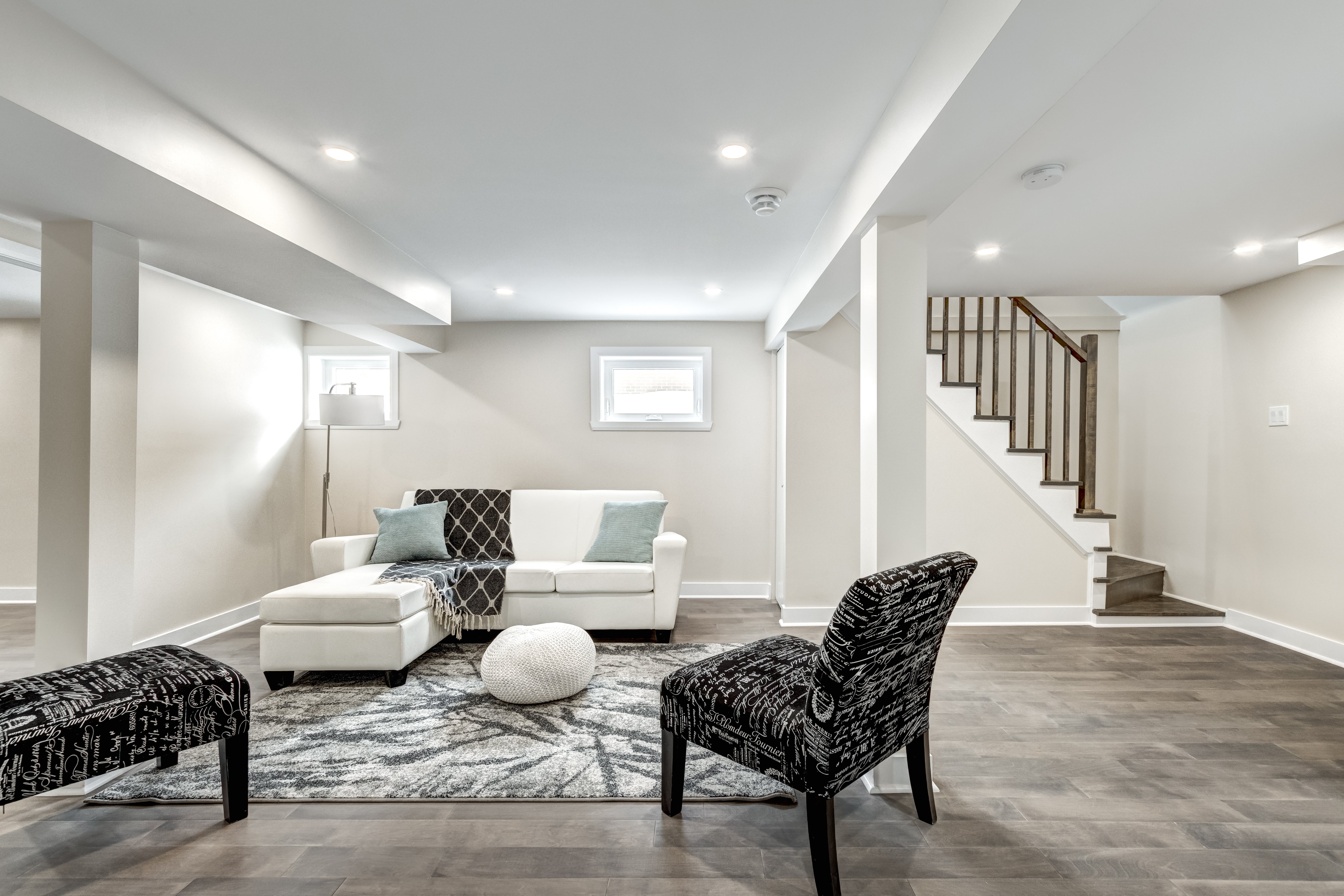 Modern living room with white sofa, black armchair, and staircase in the background.