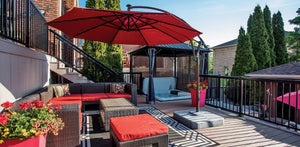 A cozy patio with a red umbrella, wicker sofas with red cushions, potted flowers, and a hot tub under a gazebo, surrounded by Regal Rail 6' Straight Pickets in Textured Black (FOR 42") from Regal Rail and tall green trees.