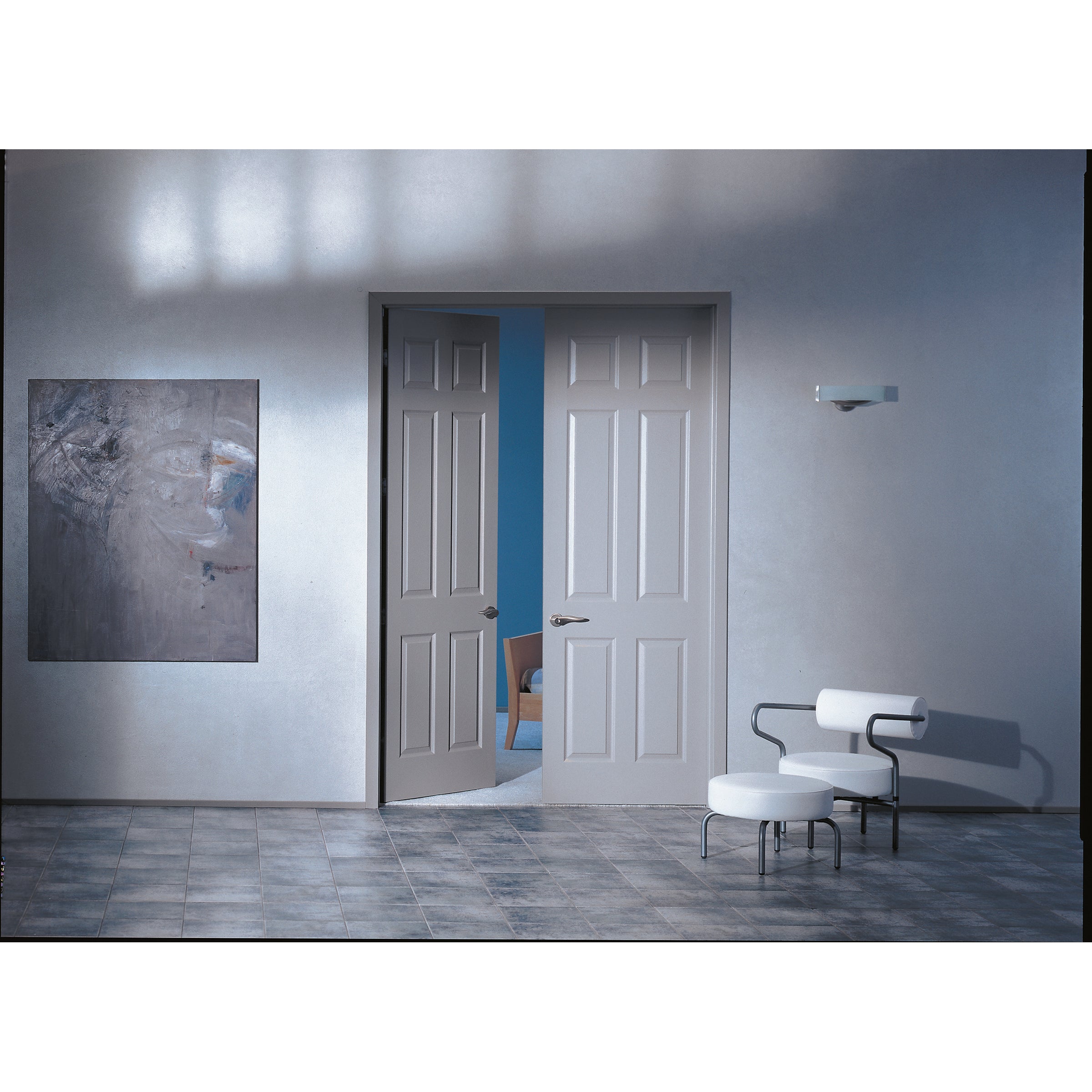 A modern room features partly open Jeld-Wen Colonist 6-Panel Textured Slab double doors (24"x96"x1-3/8"), revealing blue walls, a white armchair with black arms, matching stool, tiled floor, and abstract wall art.