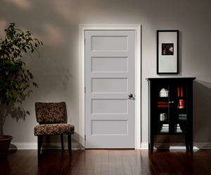 A Jeld-Wen 12"X80"X1-3/8" Conmore 5-Panel Recessed Slab door is centered in the room, with a patterned chair left, tall black cabinet with books and decor right, a plant in the corner, and a framed photo above the cabinet.