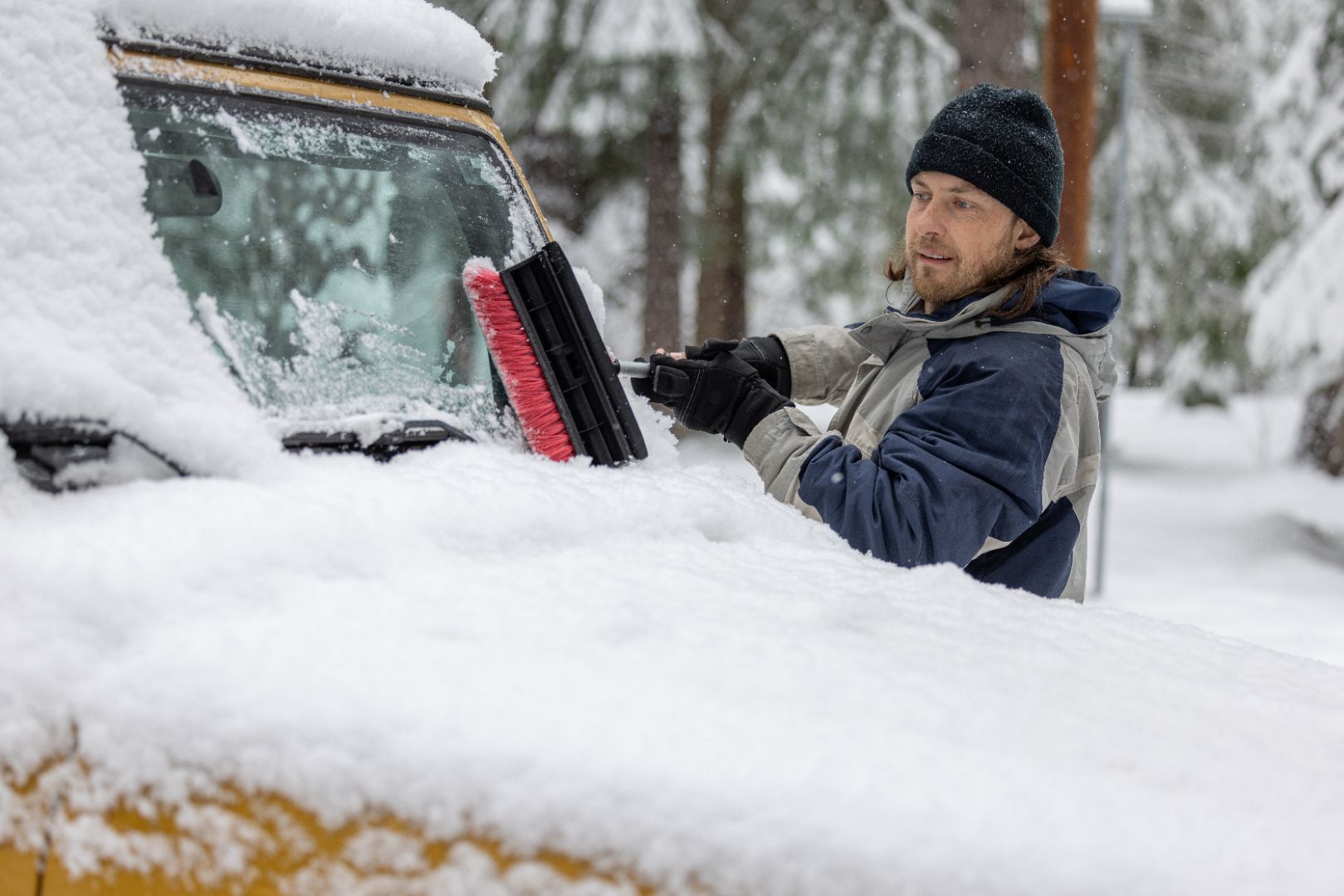 A man using a snow brush to clear snow off of his car