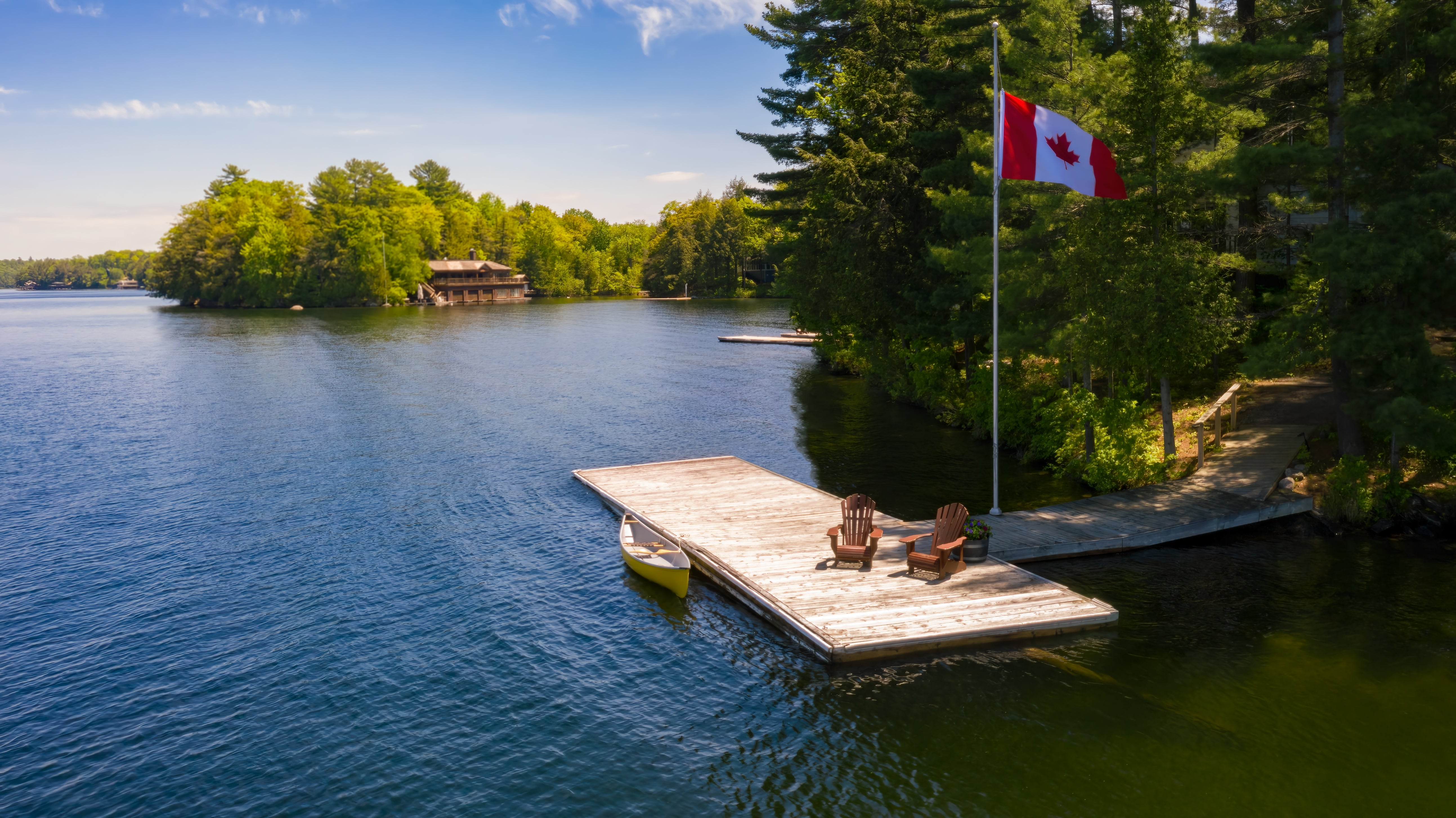 Dock with chairs and a Canadian flag on a lake surrounded by trees