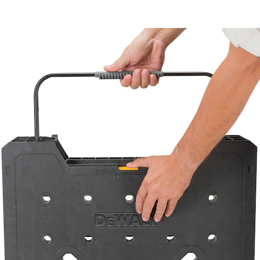 A person carries a black TurkstraLumberLtd Dewalt Folding Workbench by its handle with one hand, while the other hand rests on the top edge—ready to set up a portable workspace or tackle projects on any heavy-duty workbench.