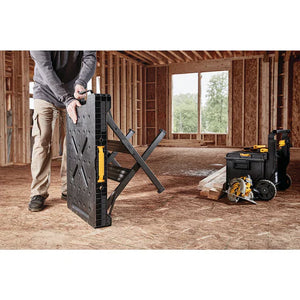 A person unfolds the Dewalt Folding Workbench from TurkstraLumberLtd in a partially constructed wooden room, with tools and lumber nearby on the floor.