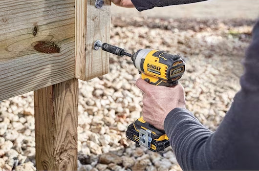 A man using a Dewalt driver to screw bolts into a deck to secure posts.