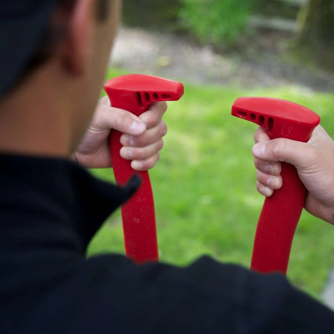 Person holding red handle for post hole digging tool with a blurred green outdoor background