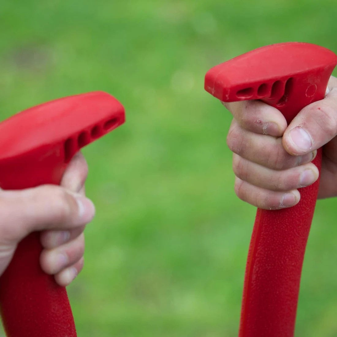 Two hands holding hole digging tool handle against a green grass background