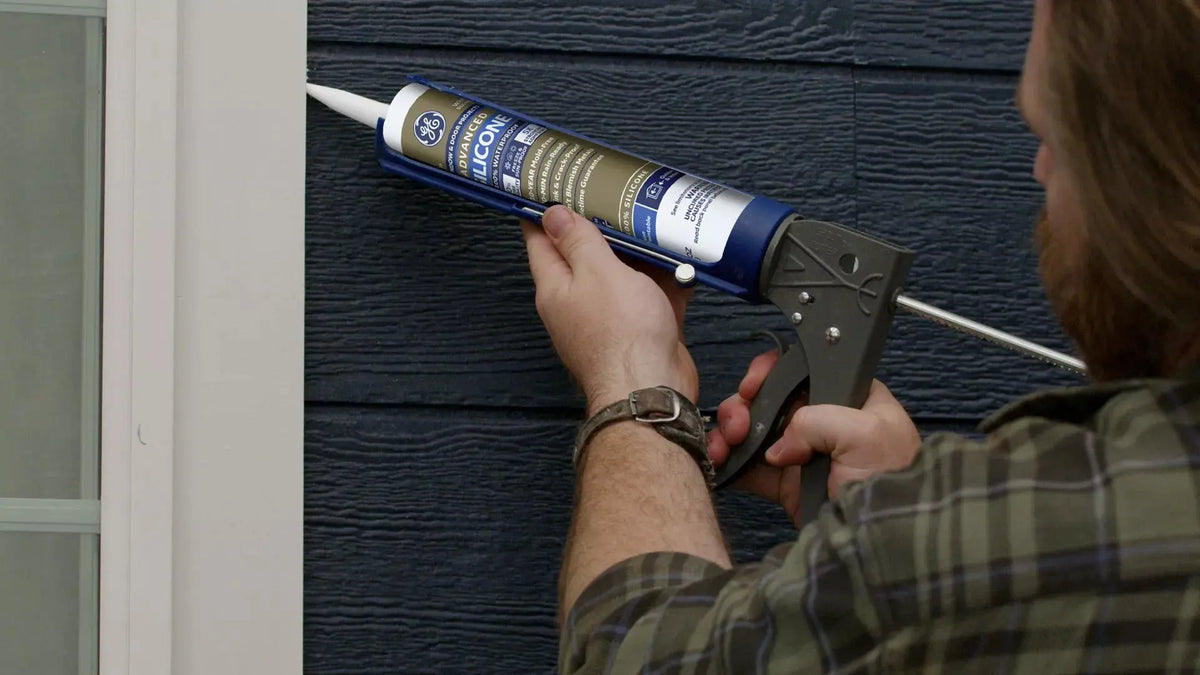 Person applying caulk to a window frame using a caulking gun.