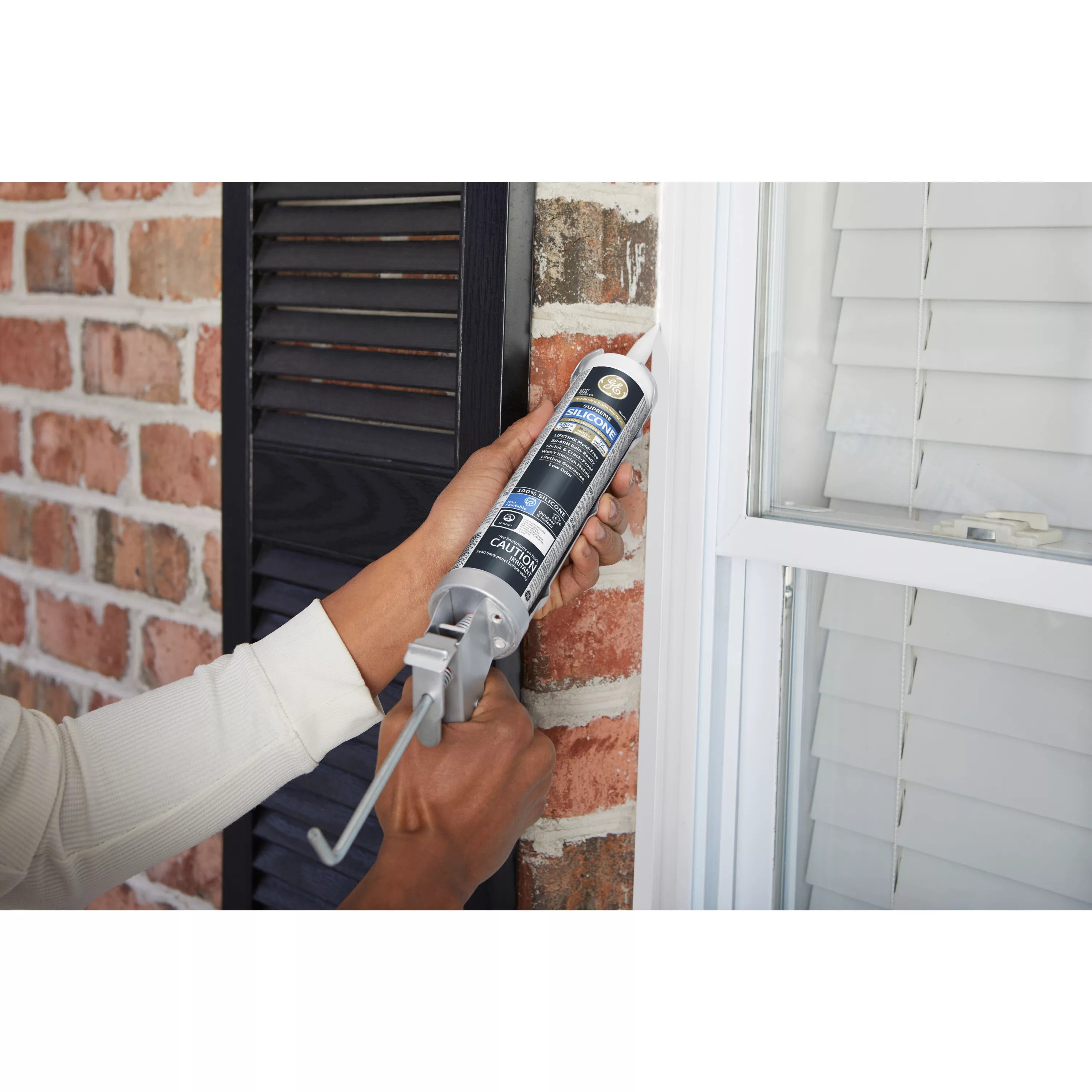 Person applying caulk to a window frame with a brick wall in the background