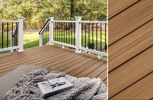 A cozy outdoor deck features Trex Enhance Naturals Golden Hour 1" x 8" x 12' composite decking with wood-like brown planks in a diagonal pattern, paired with white and black railing, all framed by trees and grass.