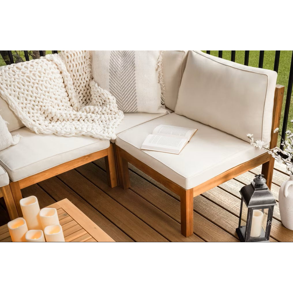 A cozy patio nook features cream cushions, a knit throw, and candles atop low-maintenance Trex Enhance Naturals Golden Hour decking by Trex; black railing and lush greenery accent the background.