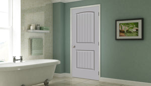 A modern bathroom with a white bathtub, light green walls, a Jeld-Wen 12"x80"x1-3/8" Santa Fe 2-Panel Slab door, a glass shelf for towels and supplies, and a framed nature photo on the wall.