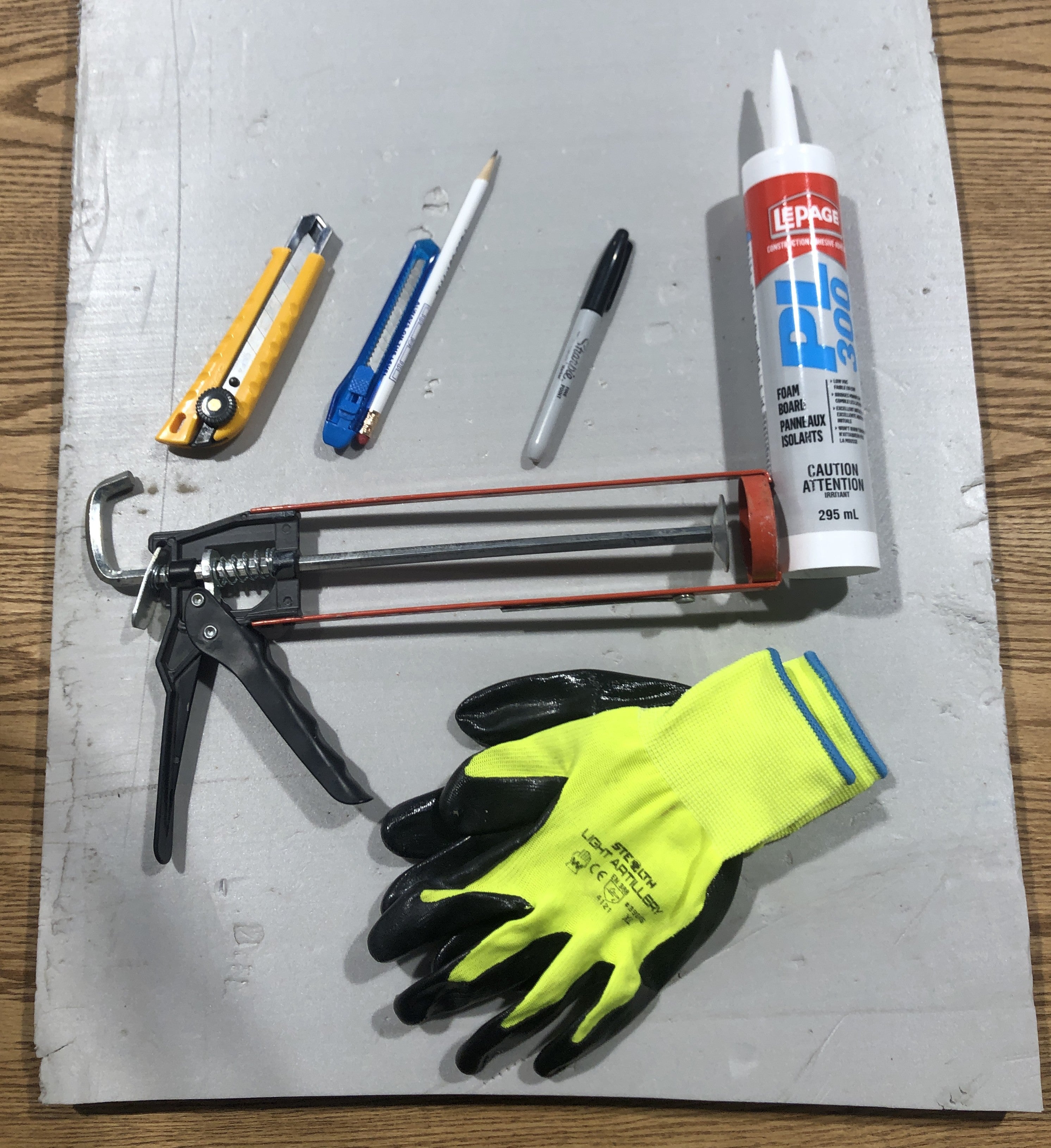 Tools and materials including a caulking gun, gloves, and sealant on a metal surface.