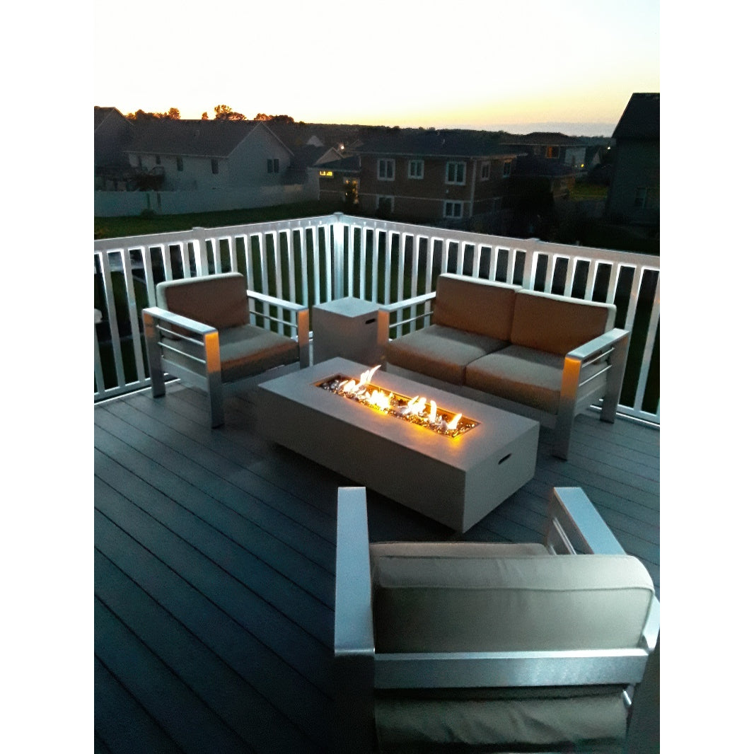 Modern patio furniture surrounds a rectangular fire pit on a deck with Regal Rail 6' Straight Pickets, White (FOR 42") by Regal Rail, at sunset, with softly lit houses and sky in the background.