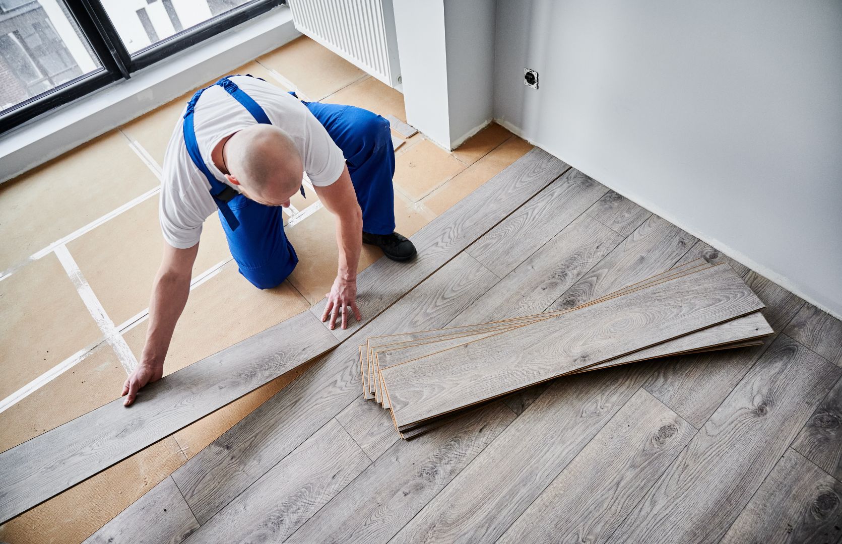 A male construction worker installing grey laminate flooring.