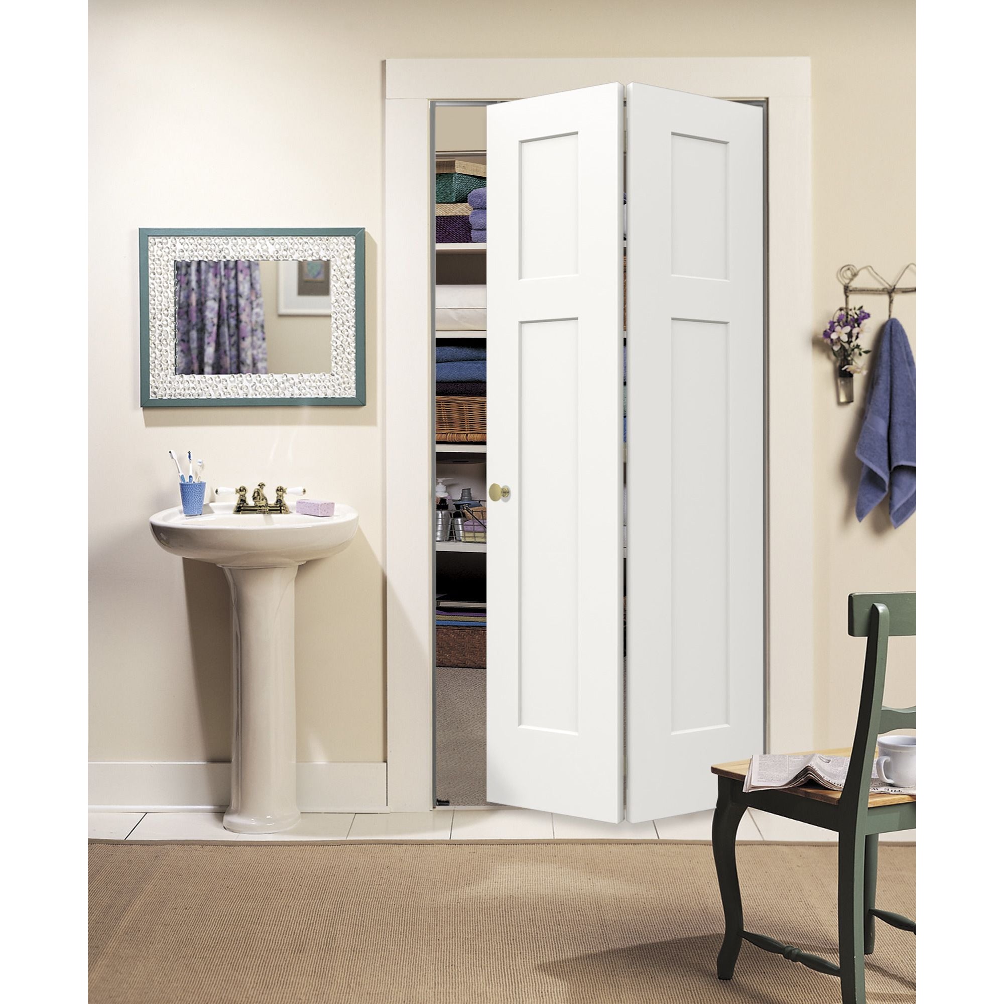 A Jeld-Wen 24"X80"X1-3/8" Craftsman 3-Panel Recessed Bifold closet door stands open to show shelves with towels and baskets. A pedestal sink with mirror is on the left, and a green chair with a towel is on the right in this tidy bathroom.