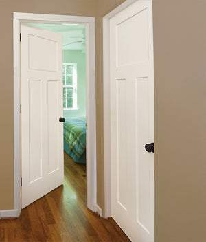 A hallway features two Jeld-Wen 12"x80"x1-3/8" Craftsman 3-Panel Recessed Slab doors—one open to a bedroom with a green and blue plaid bedspread, wooden floors, beige walls, and daylight streaming through a window.
