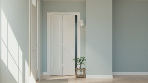 A bright, minimalist room with light blue walls, light wood floors, and a slightly open JELD-WEN 24"x80"x1-3/8" Carrara 2-Panel Square Smooth Bifold. Sunlight enters near a small plant in a wooden holder and a wall-mounted lamp.