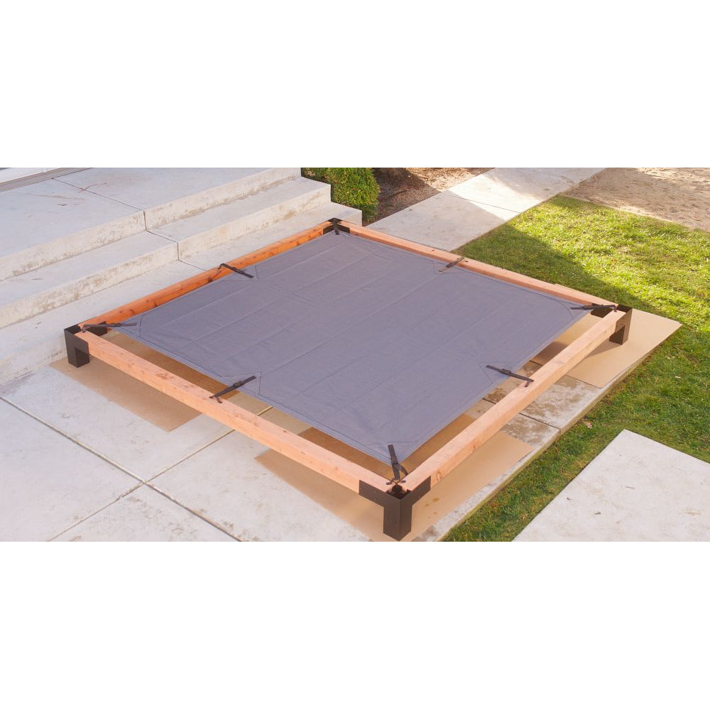 A square wooden frame assembled with Simpson Strong-Tie® Sage Corner Connector for 6x6, Black (2 per Pack), holds a gray fabric sheet above patio tiles near a grassy area. The corrosion-resistant pergola hardware and galvanized steel connectors secure the structure beside steps leading up to a small porch.