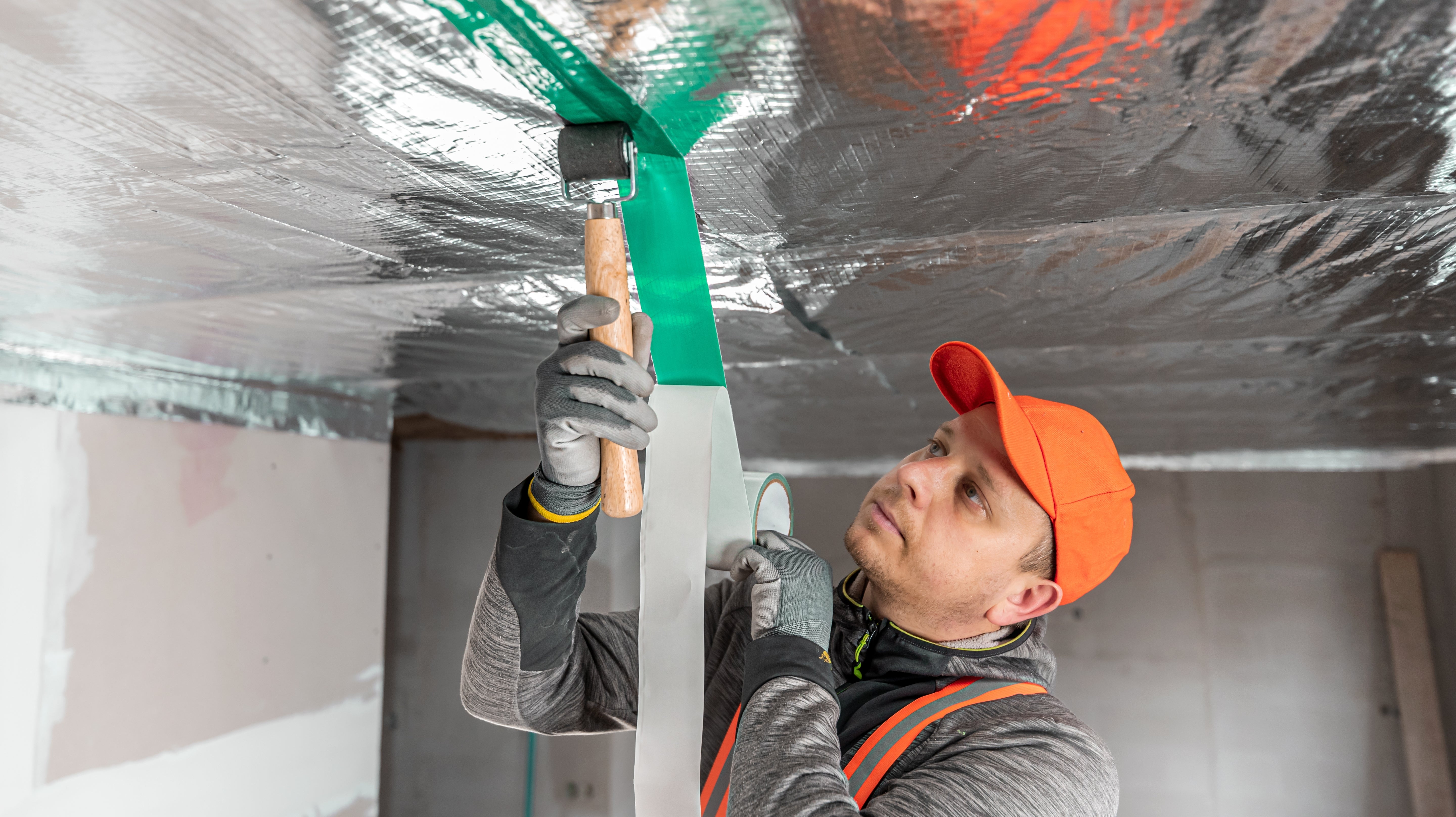 A man applying special tape to cover the joints between vapour barrier