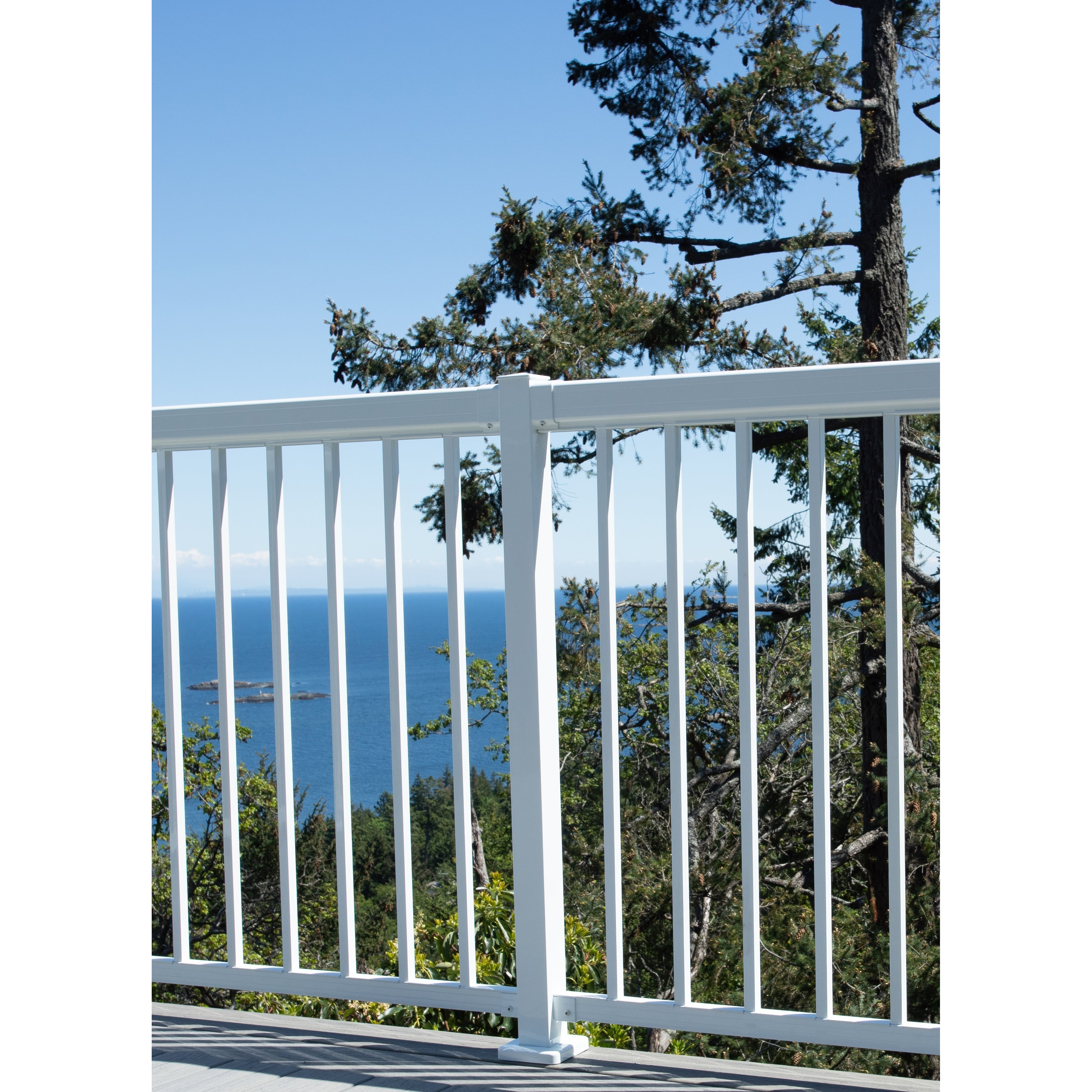 A balcony features Regal Rail 6' Straight Pickets, White (FOR 42") by Regal Rail, with sleek narrow pickets overlooking lush green trees and a scenic ocean view beneath a clear sky.