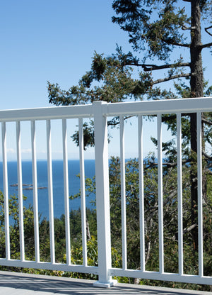 A balcony features Regal Rail 6' Straight Pickets, White (FOR 42") by Regal Rail, with sleek narrow pickets overlooking lush green trees and a scenic ocean view beneath a clear sky.