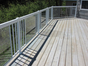 A light wood deck with Regal Rail 8' Straight Pickets, White (FOR 42") by Regal Rail, features slim white pickets and glass panels, attached to a house and overlooking a lush green yard with trees.