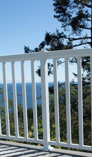 The Regal Rail Line Post in white (for 36" height) from Regal Rail creates an ideal aluminum deck railing for enjoying ocean views, distant islands, and tall trees under a clear blue sky.