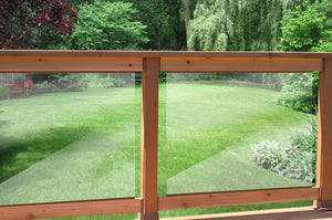 Enjoy the view from a Regal Rail balcony featuring 36-7/8"X27" clear tempered glass panels (for 42" height), overlooking a manicured lawn, lush trees, bushes, and two red chairs shaded in the background.