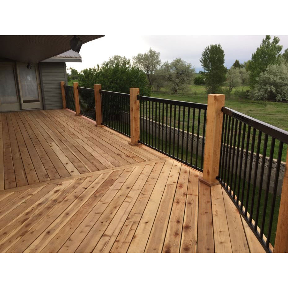 A wooden deck features Regal Rail 6' Straight Pickets, Bronze (FOR 42") by Regal Rail as a railing system, extending from a house and overlooking a grassy yard with trees beneath a cloudy sky.