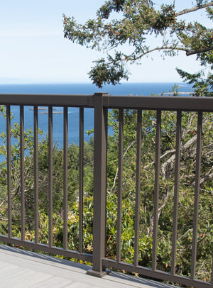 Regal Rail 6' Straight Pickets in Titanium Slate by Regal Rail are installed on a deck, overlooking lush green trees, blue ocean waters, several small islands, and a clear sky in the background.