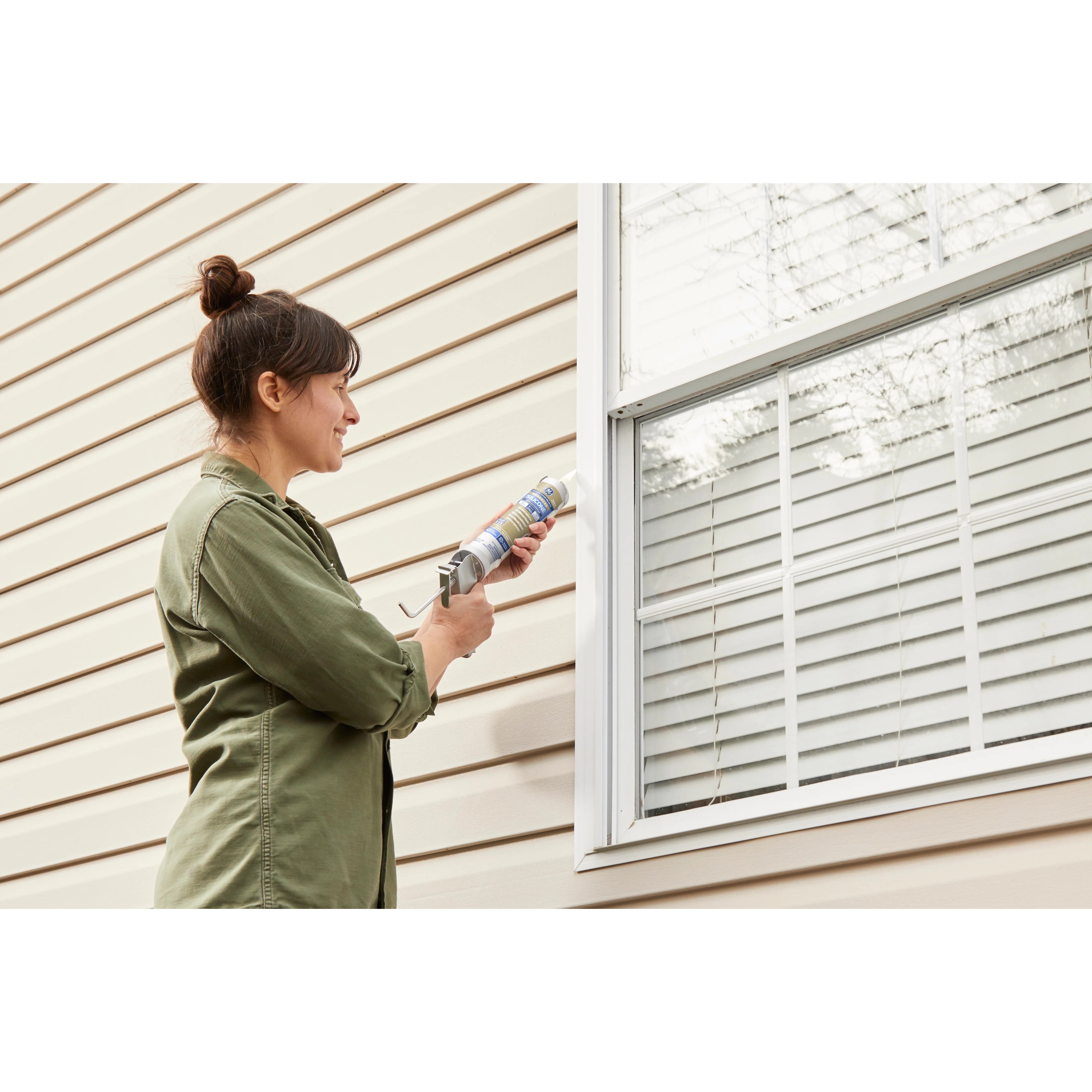 Woman applying window sealant to a house window