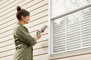 Woman applying window sealant to a house window