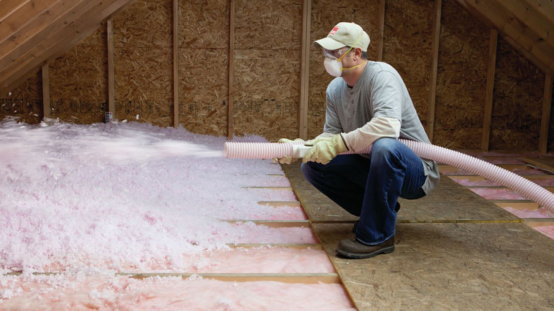 Person installing insulation in an attic with a vacuum hose.