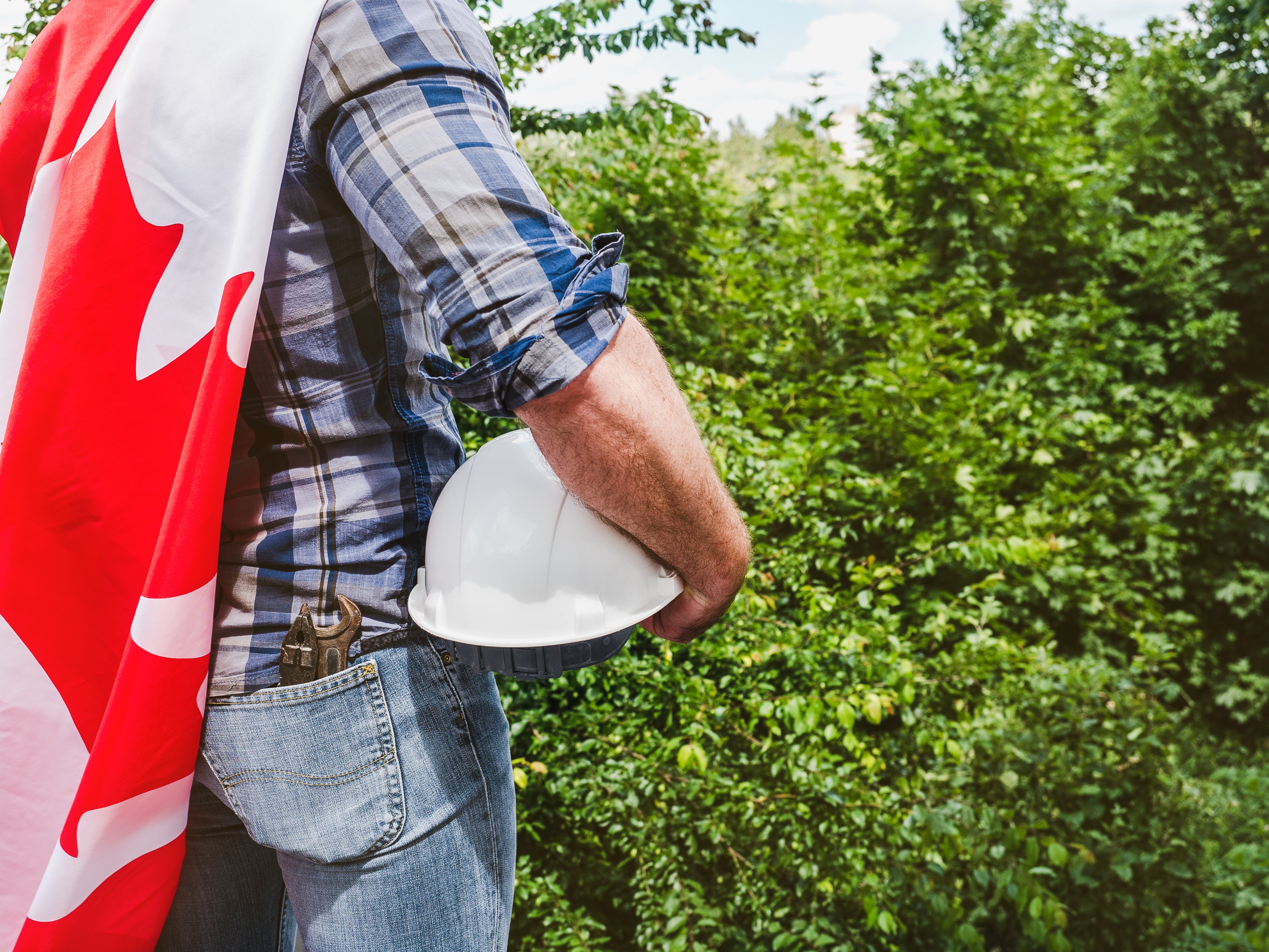 Canadian construction worker holding a white hard hat with a Canadian flag draped over his shoulder, symbolizing Labour Day and supporting Canadian-made building materials.