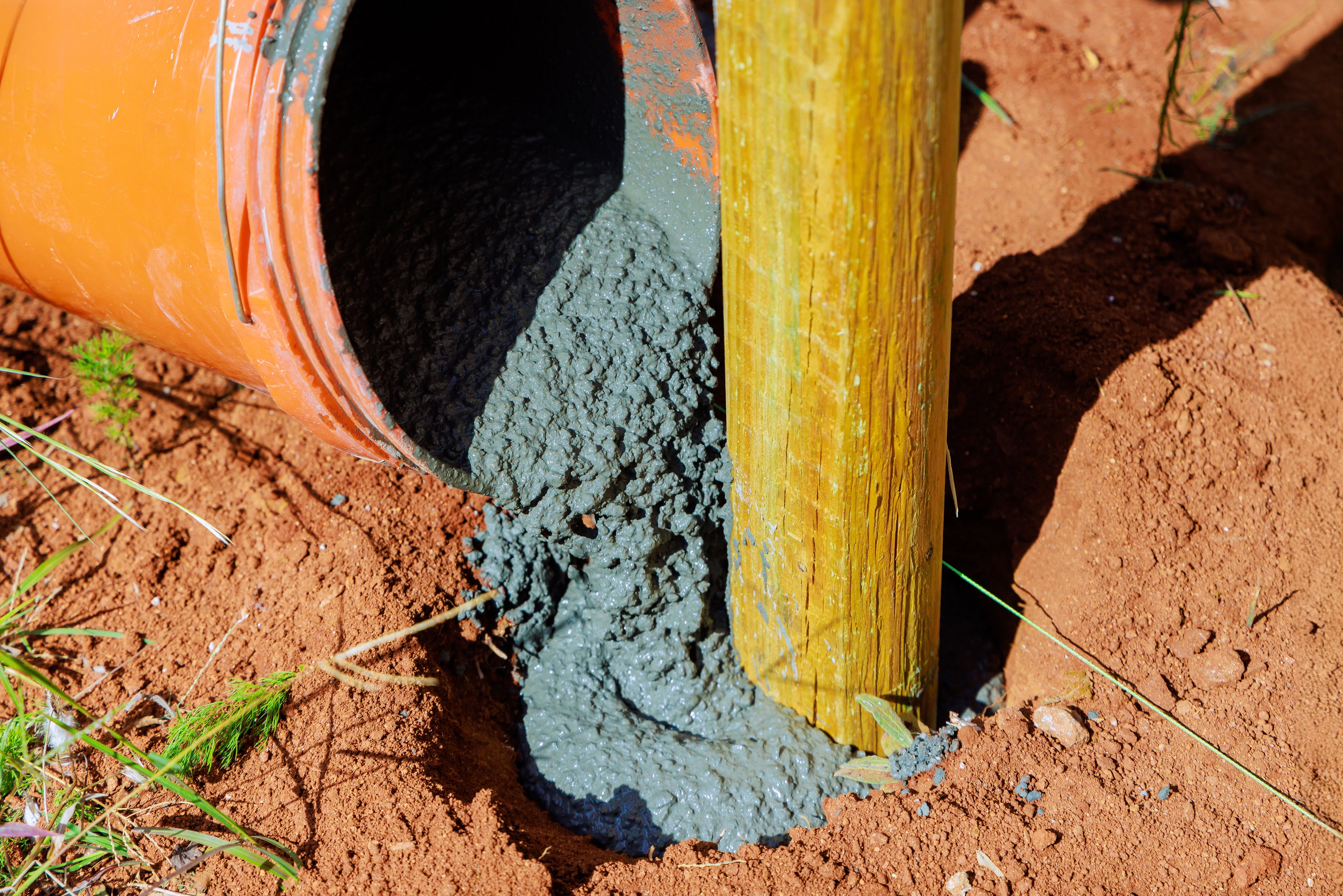 Concrete mix being poured out of an orange bucket for a fence post